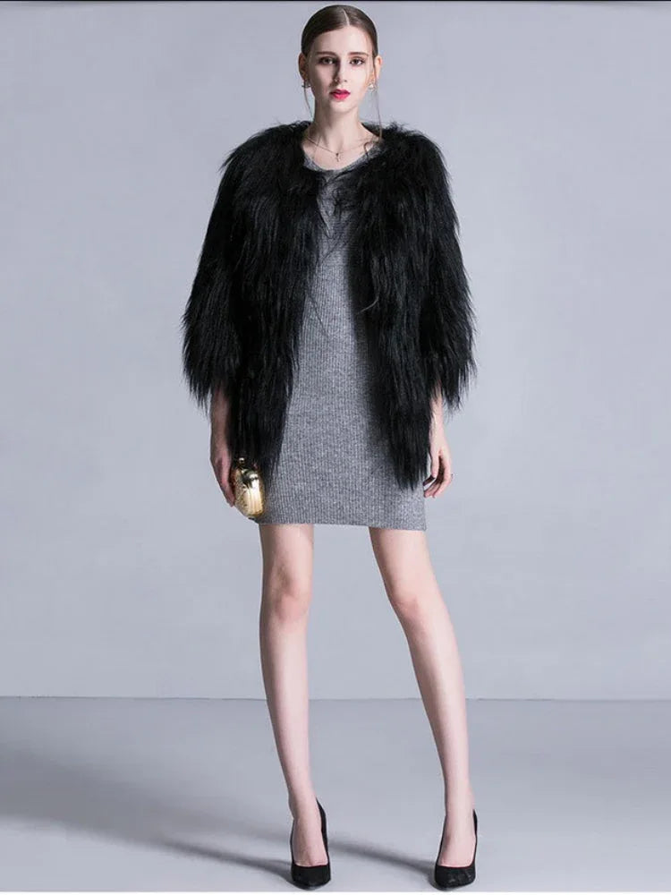 Woman wearing a black faux fur cropped jacket over a grey knit dress, holding a gold clutch. Main image