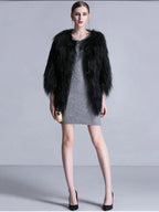 Woman wearing a black faux fur cropped jacket over a grey knit dress, holding a gold clutch.