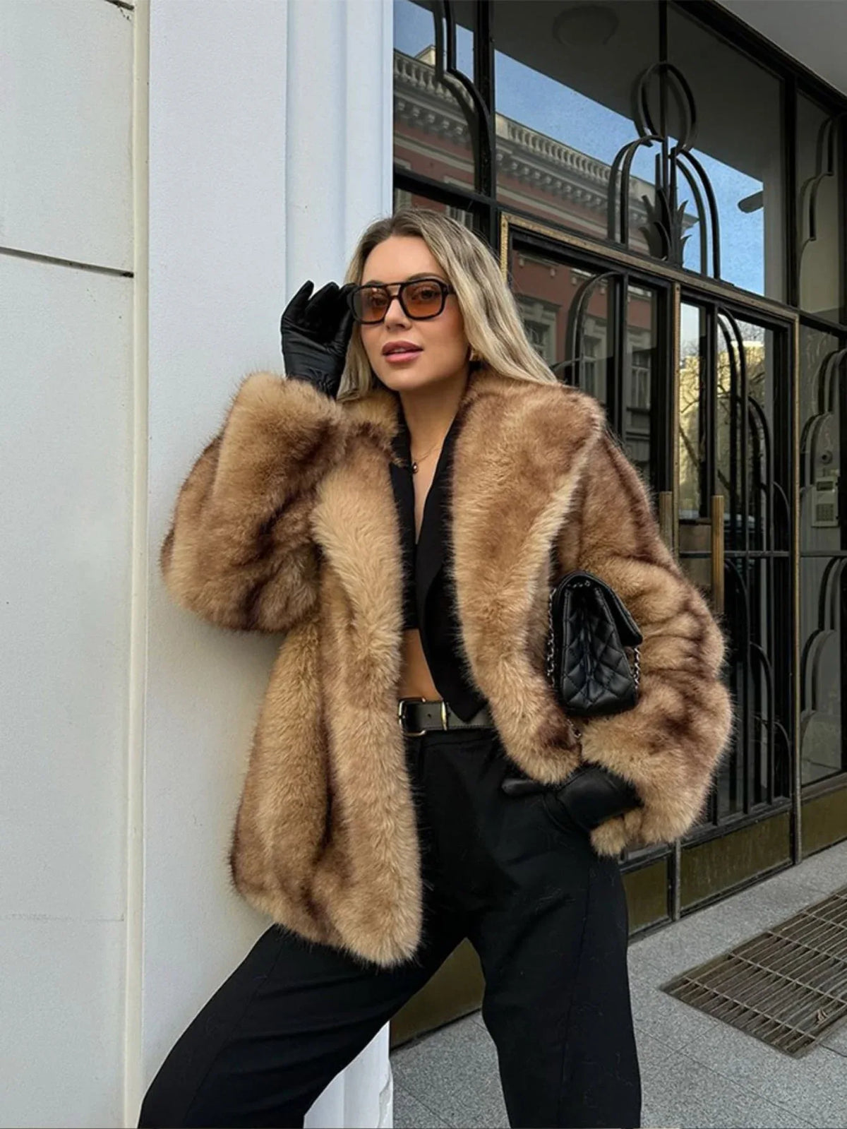 Woman wearing a tan and brown faux fur cropped jacket with black pants and black gloves.