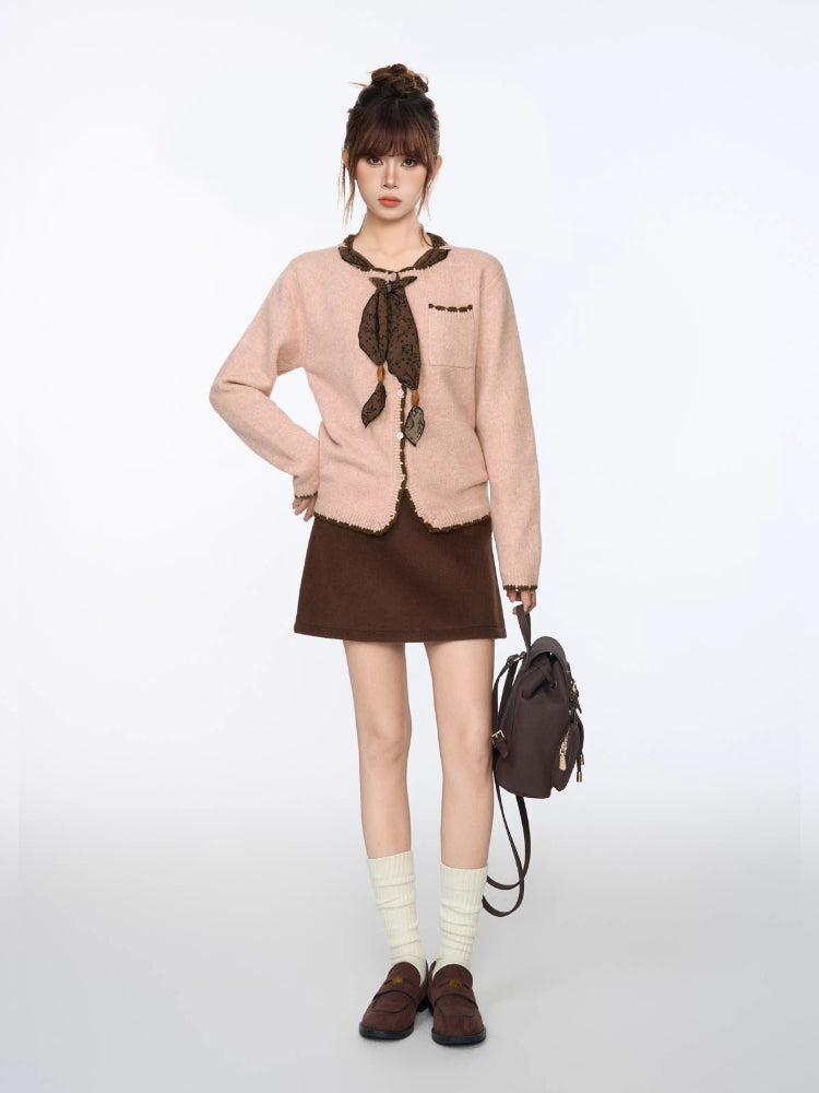 Full length shot of a model in a pink knit cardigan, brown skirt, white socks, and brown loafers.