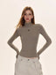 Woman wearing a taupe turtleneck top with a black embroidered cross, paired with light-colored cargo pants.