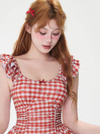 Close-up of a woman wearing a red and white gingham dress with a scoop neckline and ruffled sleeves.