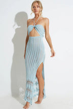 Woman wearing a light blue knit maxi dress with a halter neckline and cut-out detail, with a slit on the side.