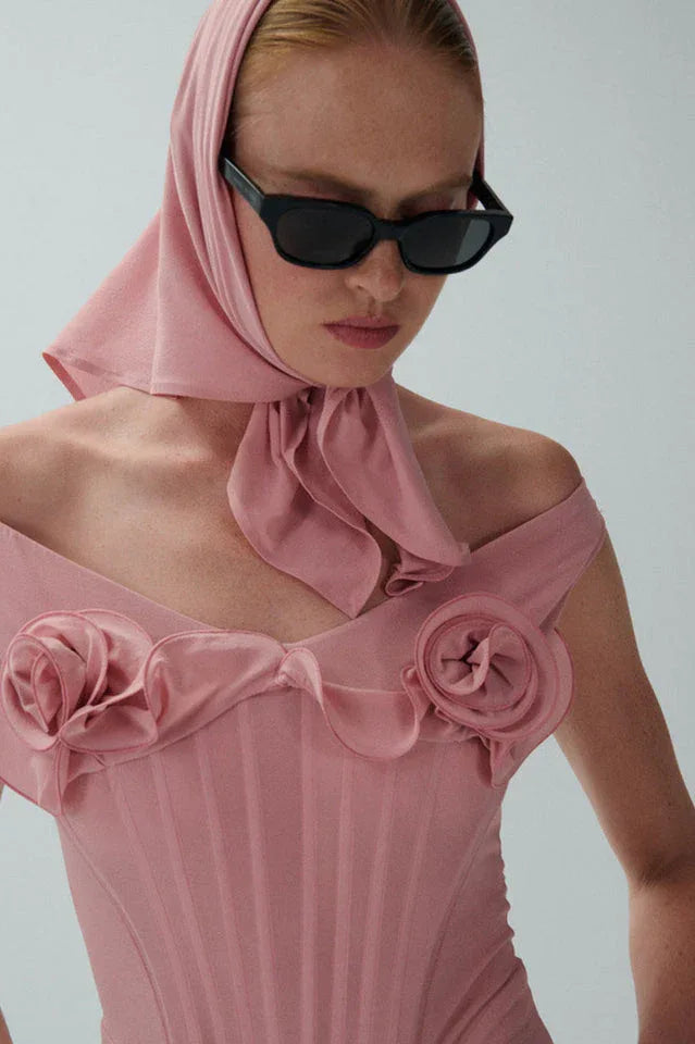 Close-up of the neckline of a pink off-the-shoulder dress featuring floral appliqués and a tie detail.
