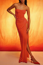 Woman wearing a strapless orange ruched gown with a high slit