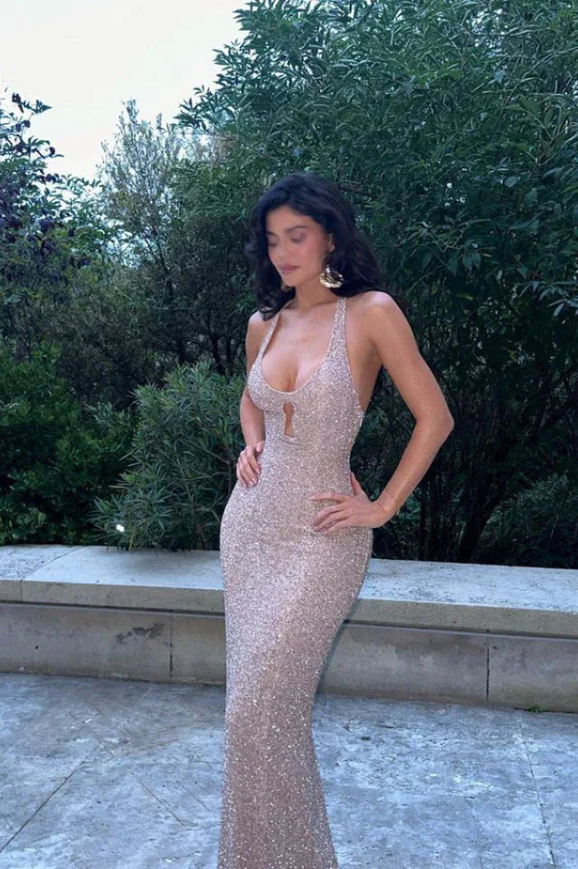 Woman in a sequined halter dress with a keyhole cutout, standing with hands on hips in an outdoor setting