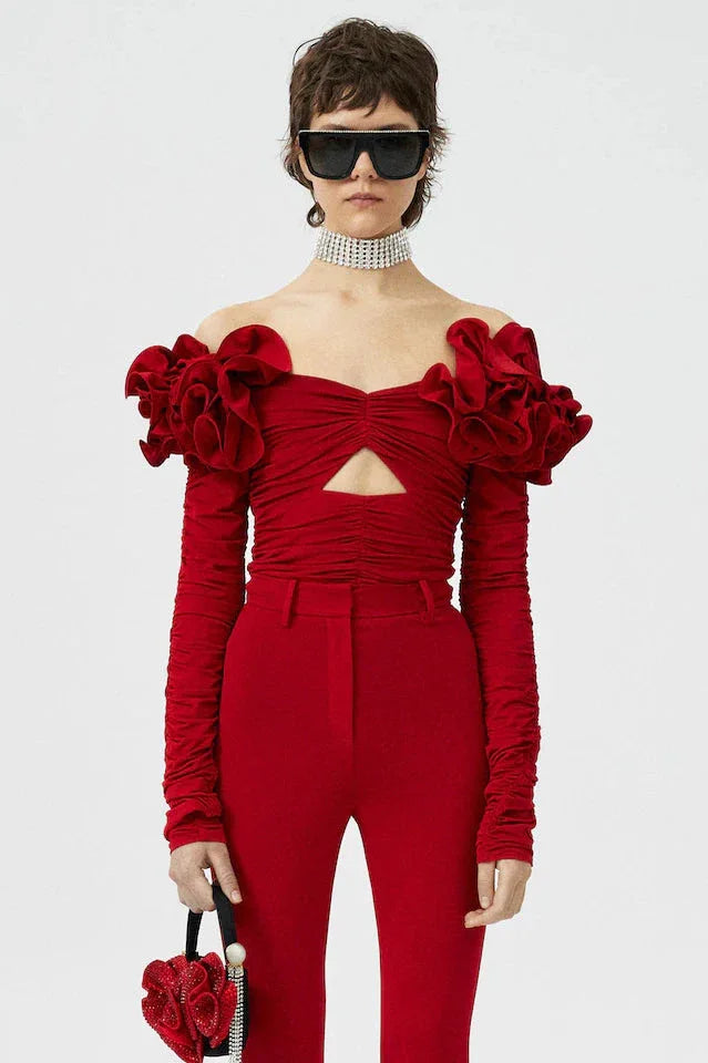 Model wearing a red off-the-shoulder top with ruffled floral shoulder details and a cutout, paired with matching red trousers and black sunglasses. Main image