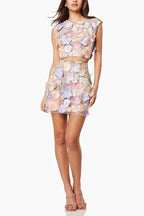 Full body shot of a woman in a floral applique crop top and mini skirt, viewed from the front.