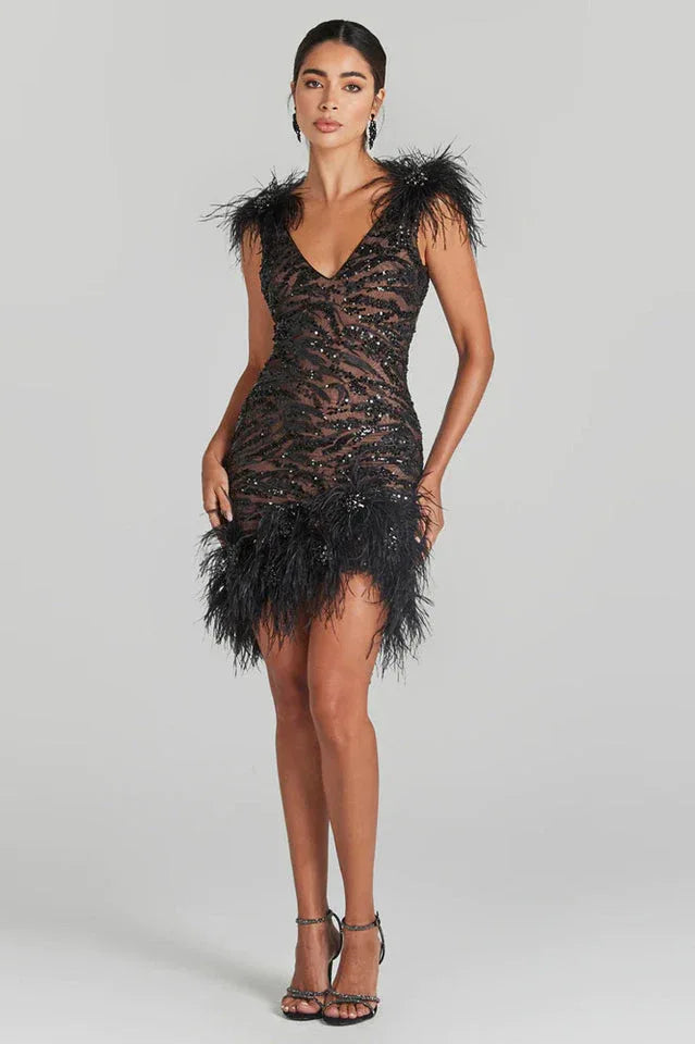 Full-body view of a woman in a black sequined mini dress with feather trim, standing and facing forward.