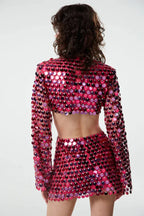 Back view of a woman wearing a pink sequined crop top with bell sleeves and a matching mini skirt with a cut-out detail at the waist.