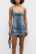 Model wearing a blue denim corset mini dress and holding a silver handbag, viewed from the front.