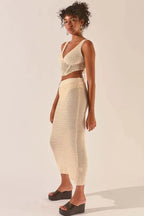 Woman wearing a cream crochet knit crop top and matching maxi skirt, side view.