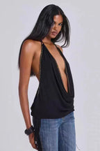 Model wearing a black halter top with a deep V-neck and studded trim, paired with blue jeans with fringe detailing.