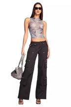 Full body shot of a woman in a marble print mesh tank top and black cargo pants holding a handbag