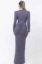Back view of a woman wearing a long, dark purple, sparkly dress with ruched detailing on the back, standing against a white background.