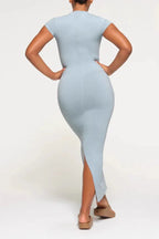 Rear view of a woman wearing a light blue full-length ribbed knit dress with short sleeves and a crew neck, showing the fitted silhouette and side slit.