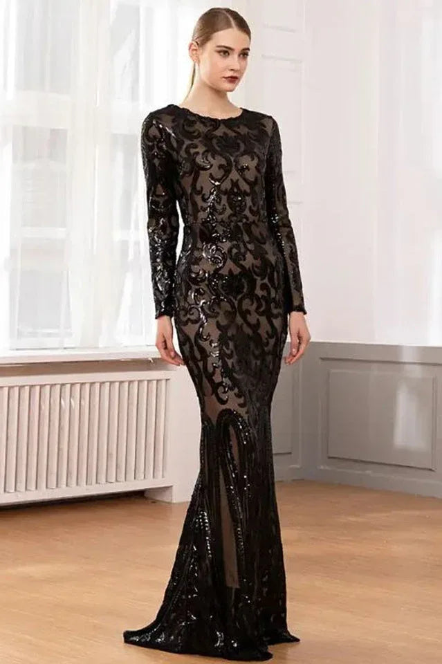 Woman in a long-sleeved, floor-length black sequined dress with a burnout pattern, standing indoors near a window.