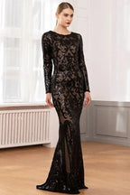 Woman in a long-sleeved, floor-length black sequined dress with a burnout pattern, standing indoors near a window.