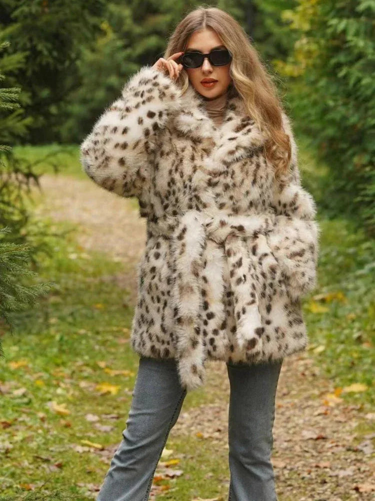 Woman wearing a spotted faux fur coat cinched with a belt, grey jeans, and sunglasses, standing outdoors on a path.