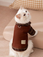 A white cat looking to the side while wearing a brown plaid shirt with a collar.
