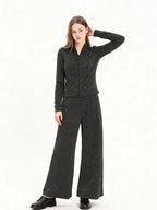 Model wearing a charcoal grey knit zip-up jacket and matching wide-leg pants, side view with hand on head.