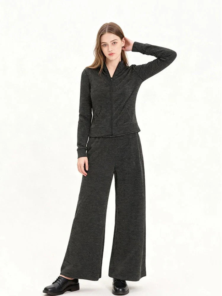 Model wearing a charcoal grey knit zip-up jacket and matching wide-leg pants, side view with hand on head.