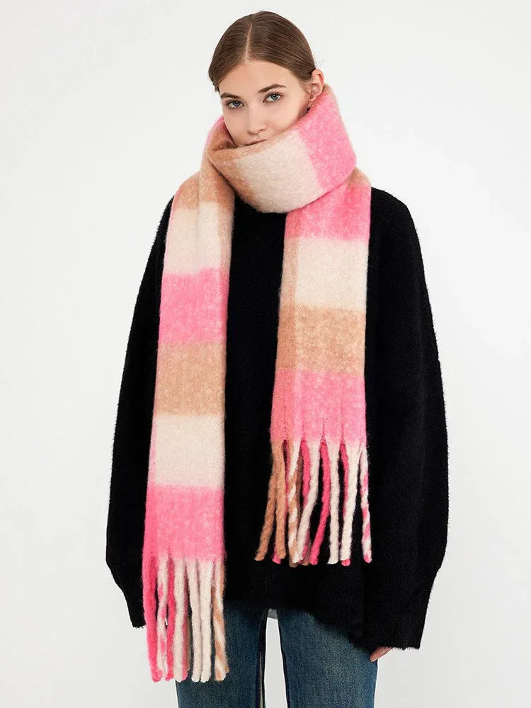 Woman wearing a black sweater and a pink and tan plaid scarf with fringe.