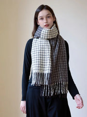 Woman wearing a black long-sleeve top and a plaid scarf with fringe detail, styled loosely around her neck.