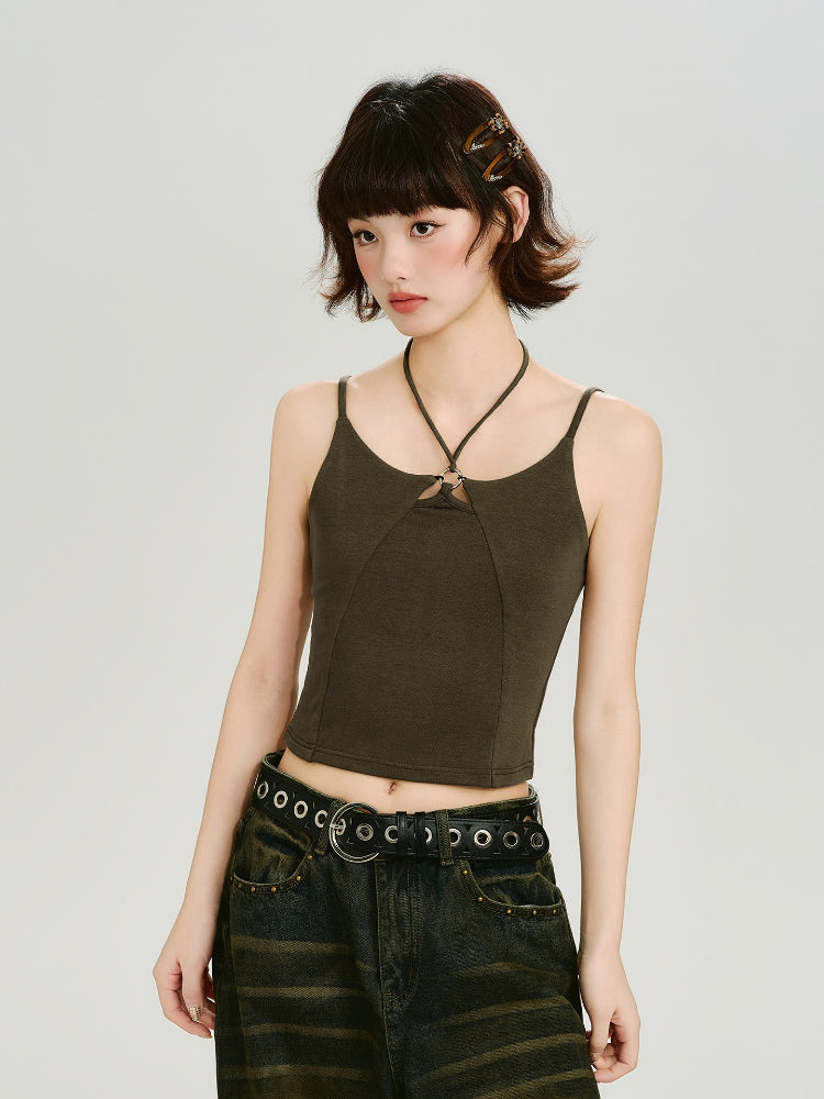 Woman wearing a dark olive green halter crop top with a ring detail at the neckline and a dark wash wide-leg jean with a grommet belt, side profile.