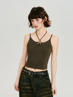 Woman wearing a dark olive green halter crop top with a ring detail at the neckline and a dark wash wide-leg jean with a grommet belt, side profile.