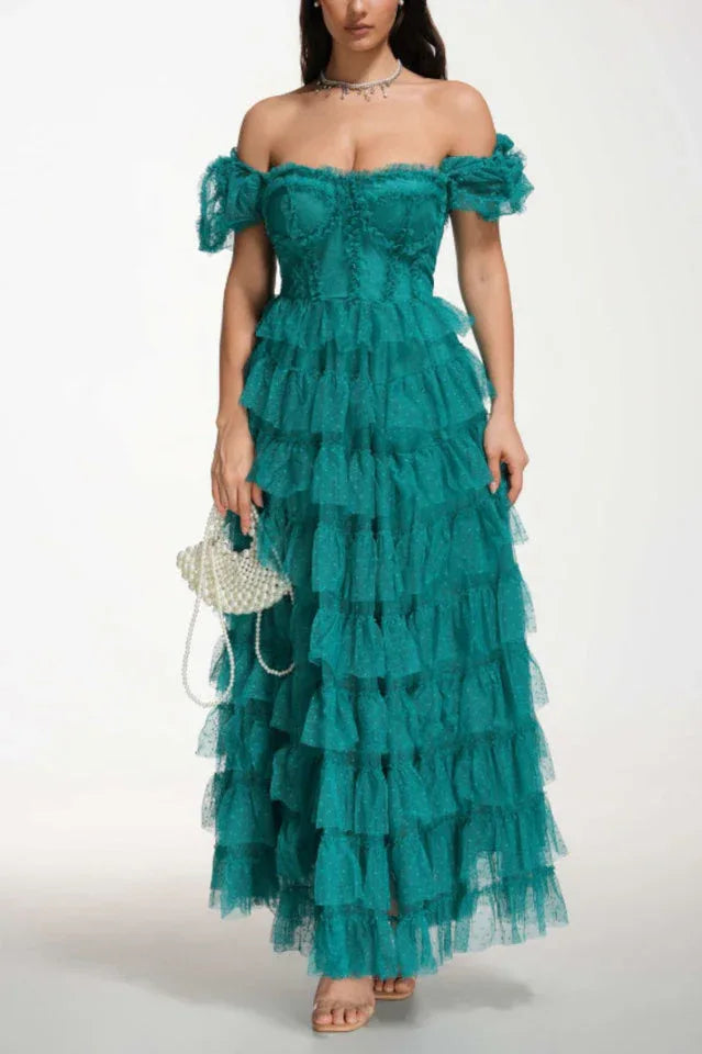 Woman wearing a formal emerald green tiered tulle gown with puff sleeves and a sweetheart neckline, holding a pearl handbag.