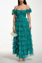 Woman wearing a formal emerald green tiered tulle gown with puff sleeves and a sweetheart neckline, holding a pearl handbag.