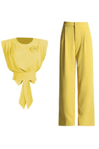 A yellow cropped top with a rose embellishment and bow detail, shown next to a pair of yellow wide-leg pants.
