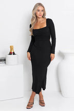 Woman wearing a black long-sleeved midi dress with a square neckline and side slit, viewed from the front