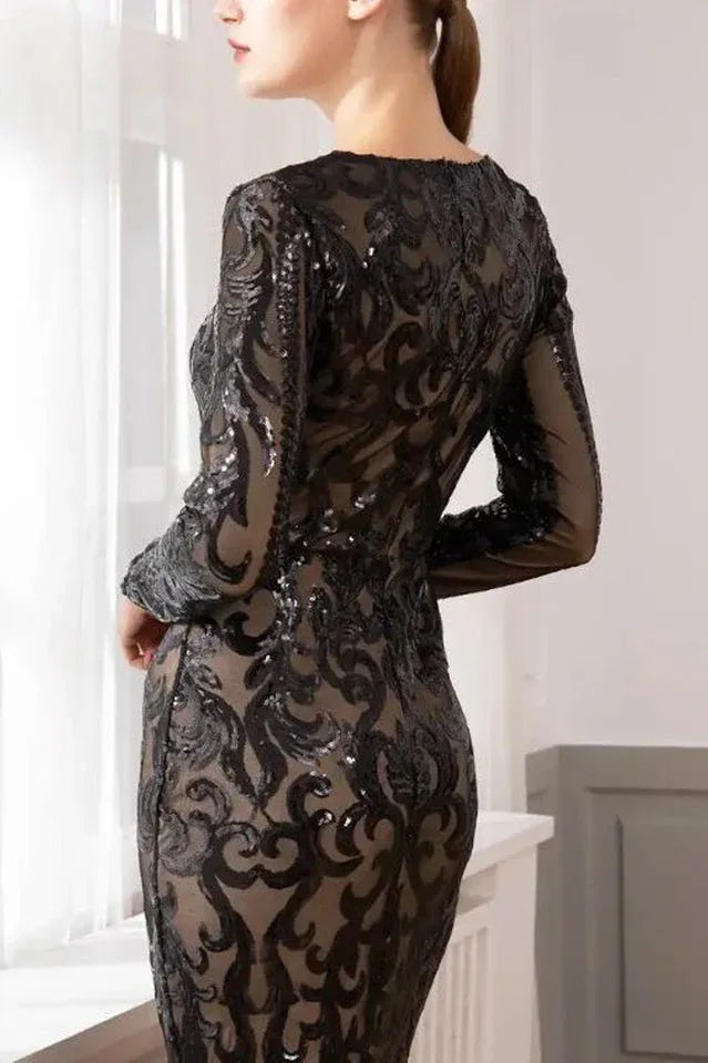 Back view of a woman in a long-sleeved, floor-length black sequined dress with a burnout pattern.