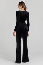 Back view of a woman in a black velvet jumpsuit with a square neckline and flared legs.