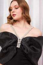 Detailed shot of the crystal-embellished neckline and bow on a black formal gown