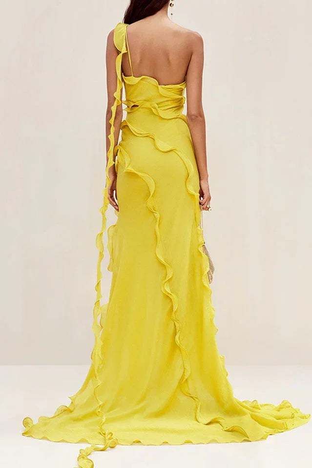 Rear view of a model in a flowing yellow one-shoulder chiffon gown with ruffled accents and a train.