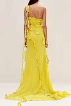 Rear view of a model in a flowing yellow one-shoulder chiffon gown with ruffled accents and a train.