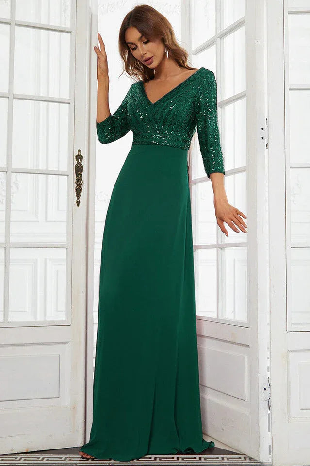 Woman wearing a floor-length emerald green sequined formal gown with 3/4 sleeves, standing in a doorway.
