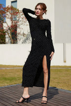 Side view of a woman in a long-sleeved black dress with feather details and a high slit.