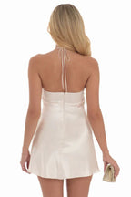 Back view of a woman in a cream satin halter mini dress, showing the zipper closure and halter ties.