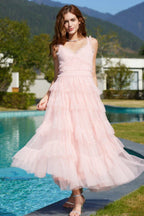 Full length shot of a woman in a light pink tiered tulle dress with a v-neckline, standing by a pool.