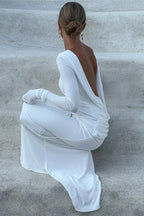 Rear view of a woman in a white draped dress with long sleeves, sitting on steps.