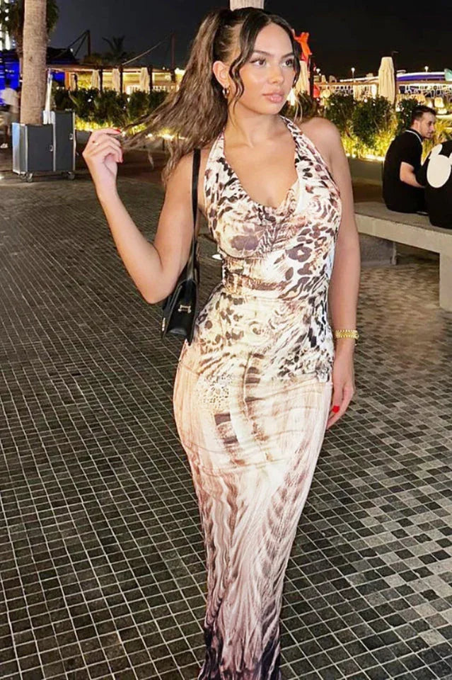 Woman wearing a sleeveless, halter-neck, abstract print maxi dress with a plunging neckline, standing outdoors at night.