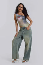Woman posing in a one-shoulder sequined top with a graphic print and light wash wide-leg jeans.