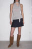 Woman wearing a grey halter top, a black pleated mini skirt, and brown knee-high boots.