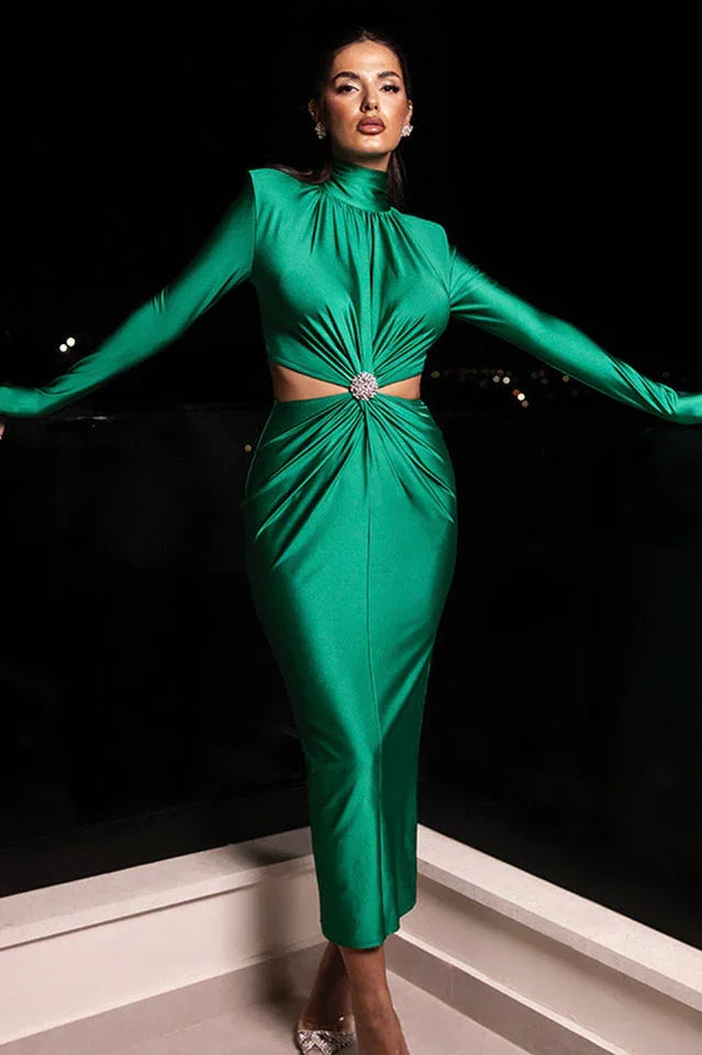 Woman wearing a long-sleeved green satin dress with a cut-out waist and embellished detail, standing outdoors at night. Main image