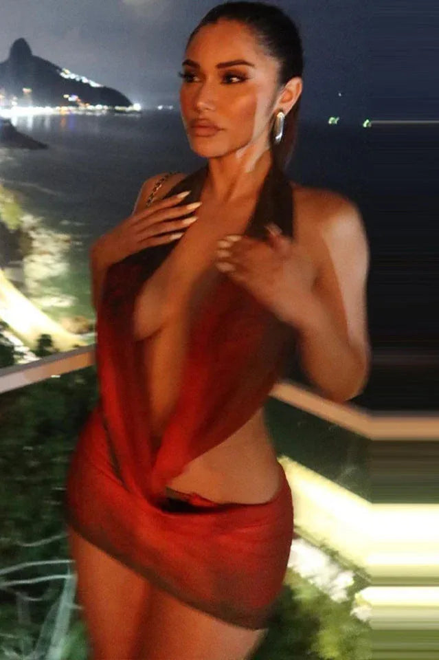Woman in a red and black sheer mesh halter mini dress with floral print, posing on a balcony at night