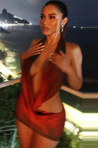Woman in a red and black sheer mesh halter mini dress with floral print, posing on a balcony at night